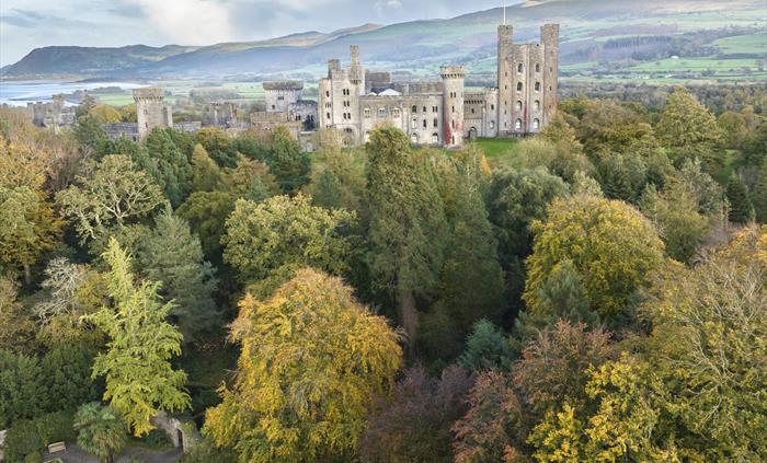 Aerial shot of Penrhyn Castle surrounded by golden and green trees in the autumn